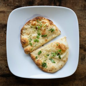 Appetizing garlic naan bread on a white plate, garnished with herbs.