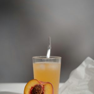 A refreshing glass of peach juice accompanied by a fresh half peach on a light textured background.