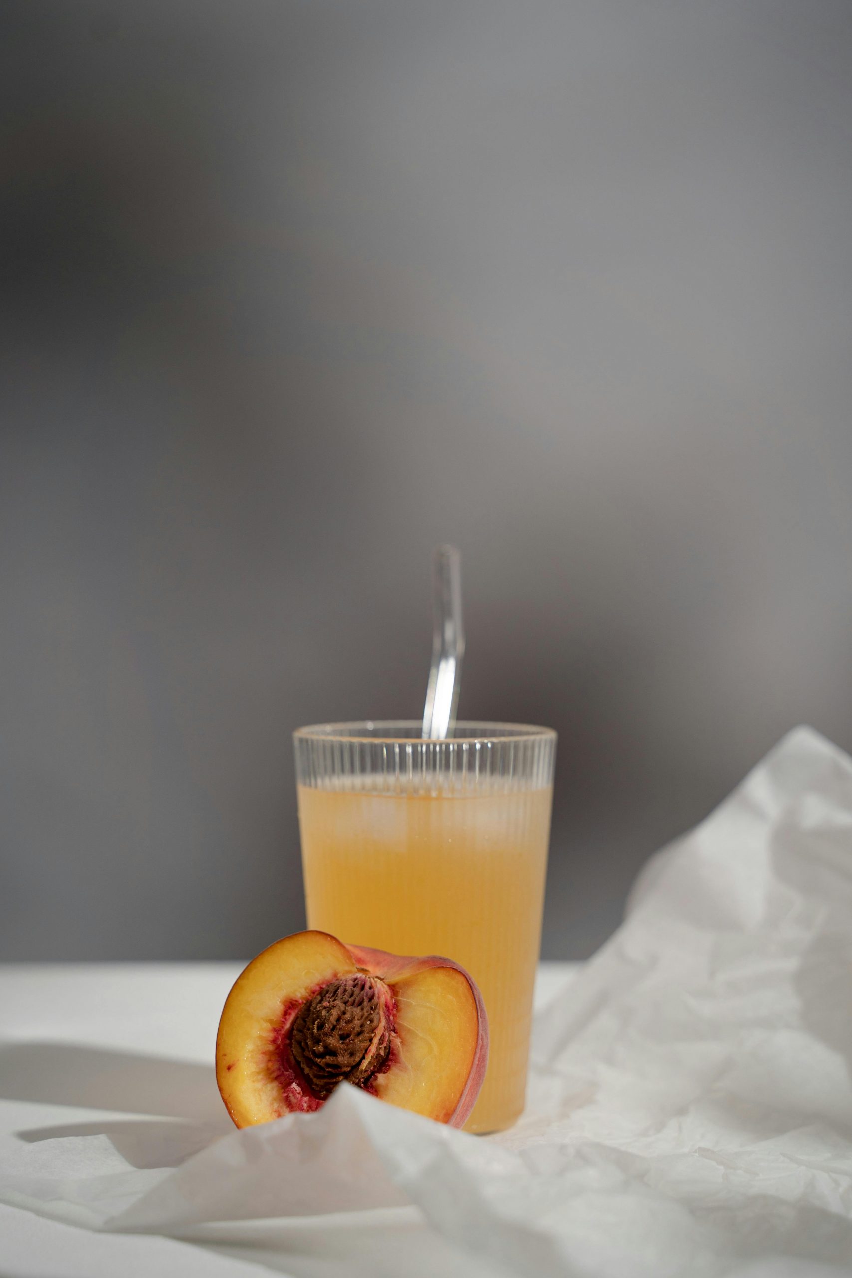 A refreshing glass of peach juice accompanied by a fresh half peach on a light textured background.