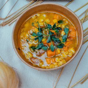 Warm bowl of vegetable soup featuring corn, carrots, and fresh herbs in an earthy setting.