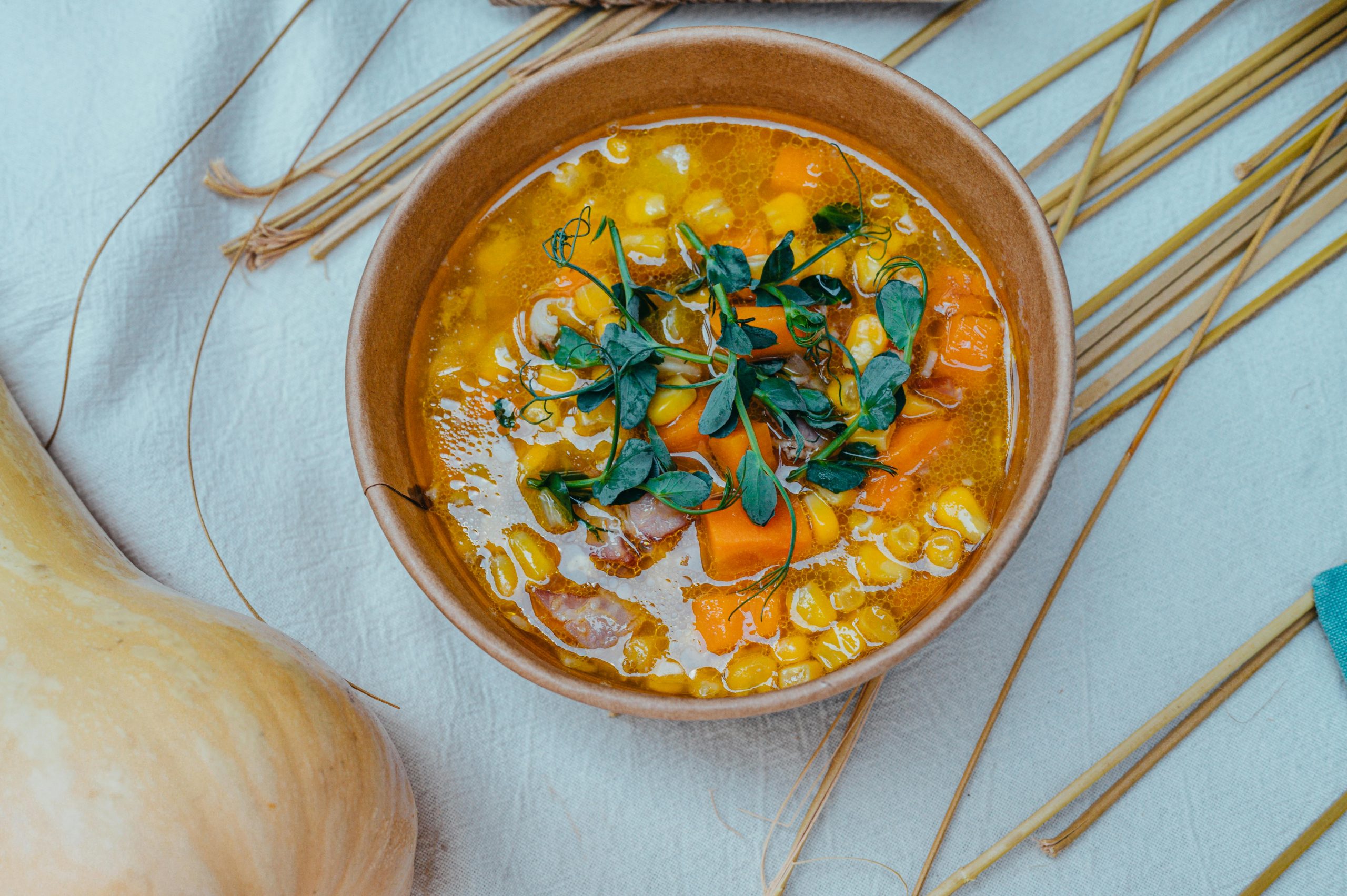 Warm bowl of vegetable soup featuring corn, carrots, and fresh herbs in an earthy setting.