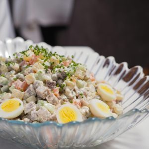 Close-up of a traditional Russian Olivier salad with eggs and chives in a glass bowl.