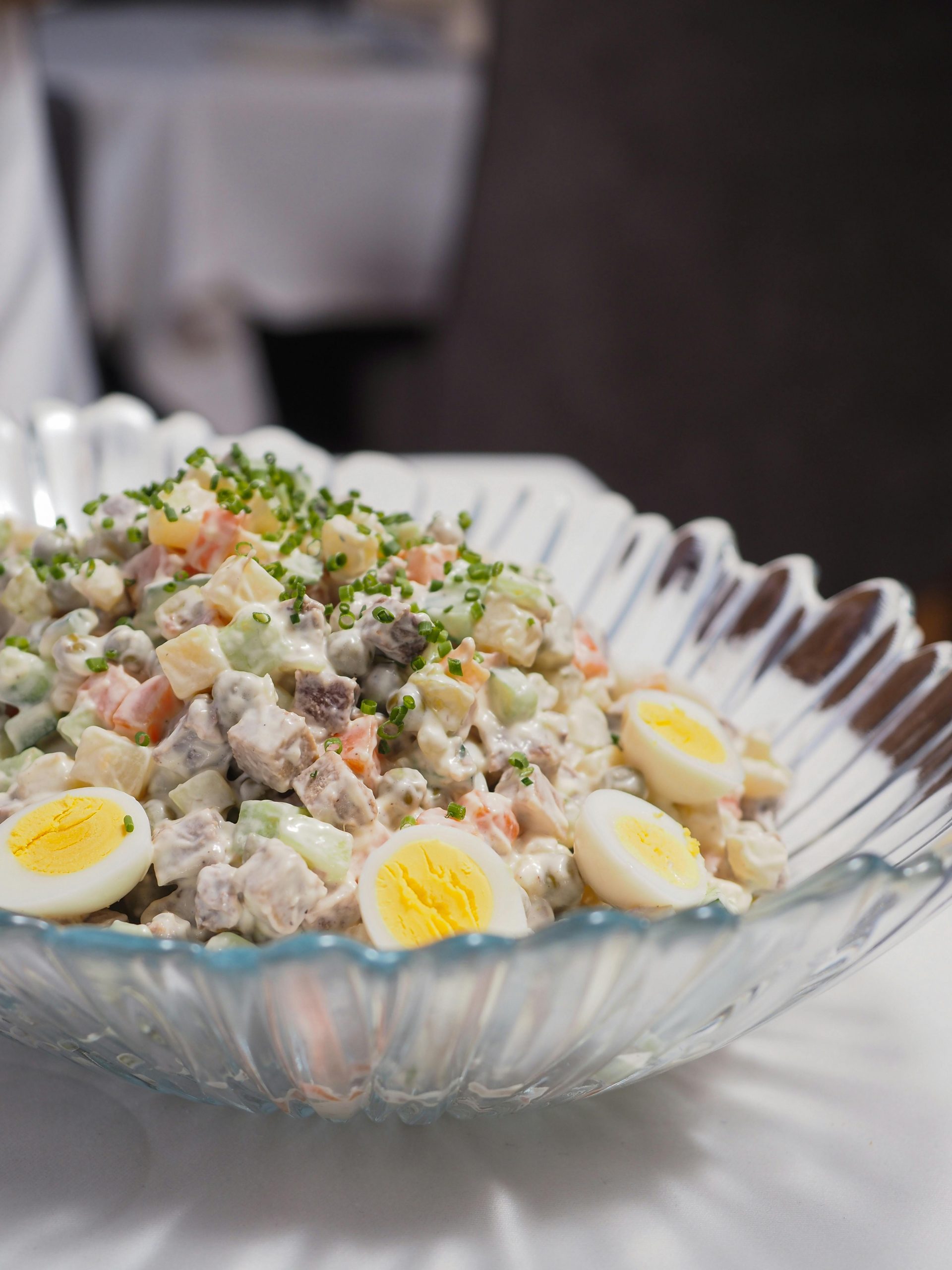 Close-up of a traditional Russian Olivier salad with eggs and chives in a glass bowl.