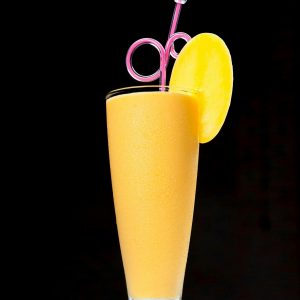 Bright mango smoothie garnished with fruit, captured in high contrast on a black background.