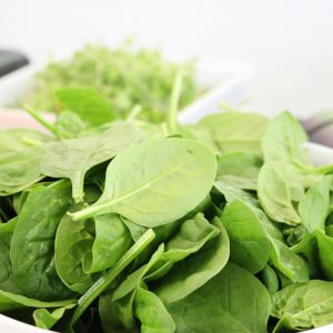 A close-up of fresh spinach leaves in a white bowl, ideal for healthy salads.