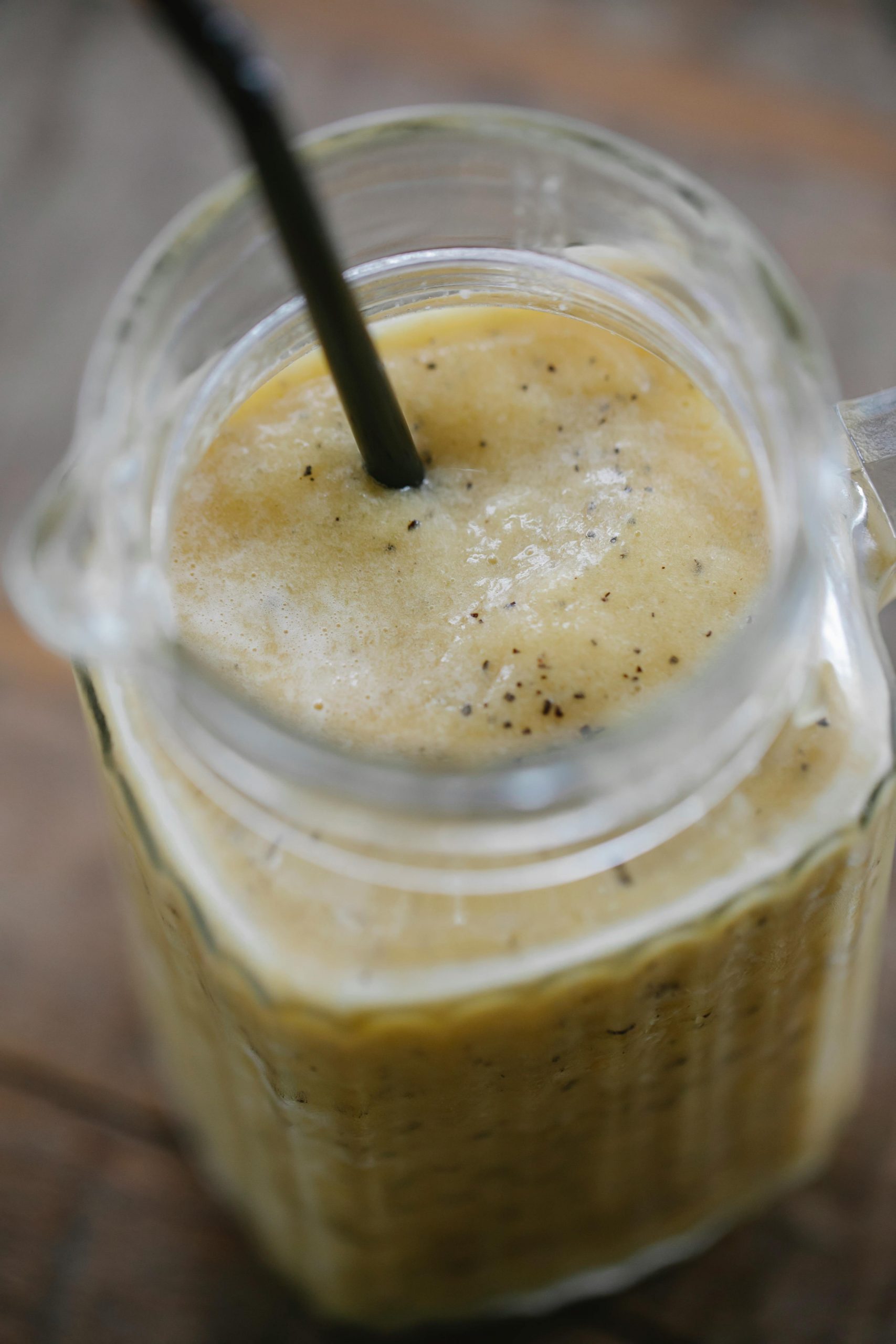 Delicious banana smoothie in a glass jug with black straw, perfect for a refreshing healthy drink.