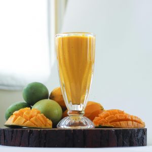 Delicious mango smoothie in a glass surrounded by fresh mangoes, perfect for a healthy refreshment.