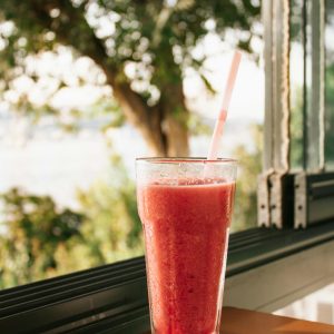 Chilled watermelon smoothie in a glass by a sunny window with a green garden view.