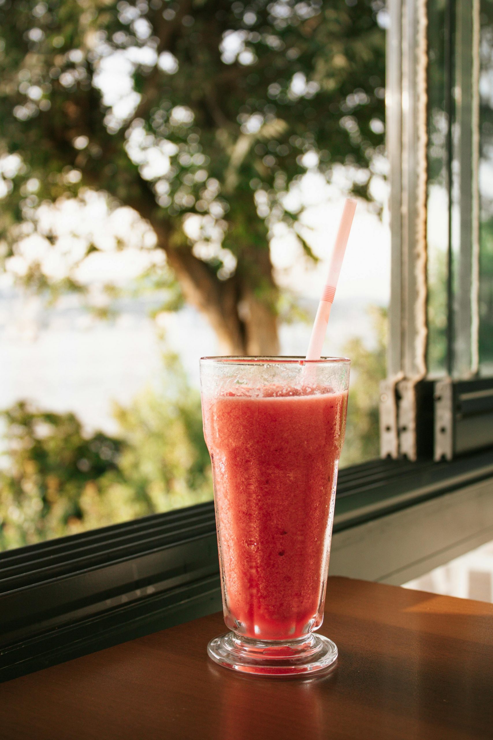 Chilled watermelon smoothie in a glass by a sunny window with a green garden view.