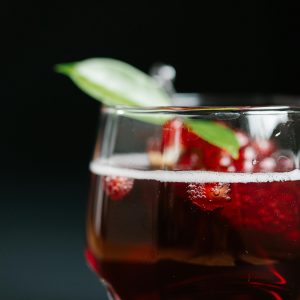 Close-up of pomegranate juice with berries and a green leaf garnish in a glass.