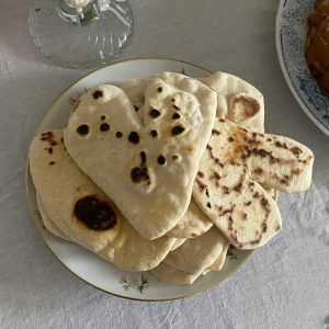 Homemade heart-shaped naan on a decorative plate with a candlelit cozy setup.